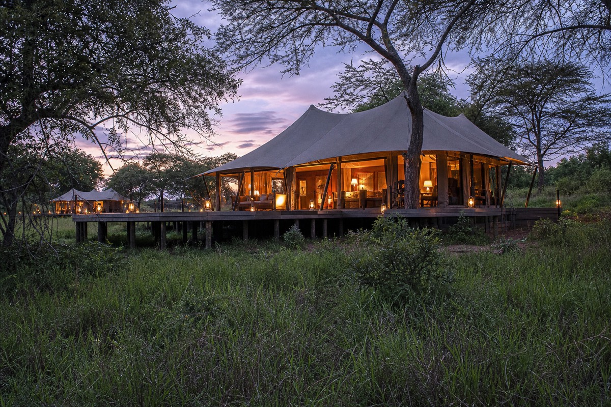 A canvas tented camp at dusk on the edge of a private conservancy bordering the Maasai Mara National Reserve